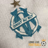 Zoom sur l’écusson brodé de l’OM avec l’étoile dorée au-dessus et l’inscription "Droit au But"